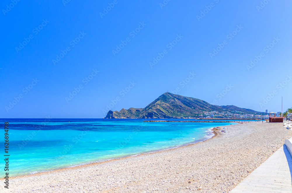 Fototapeta premium Pebbe beach in Altea town on Costa Blanca coast, mountain Sierra Helada, coastline Altea bay Mediterranean Sea with azure turquoise water in sunny day, Alicante province, Valencian Community, Spain