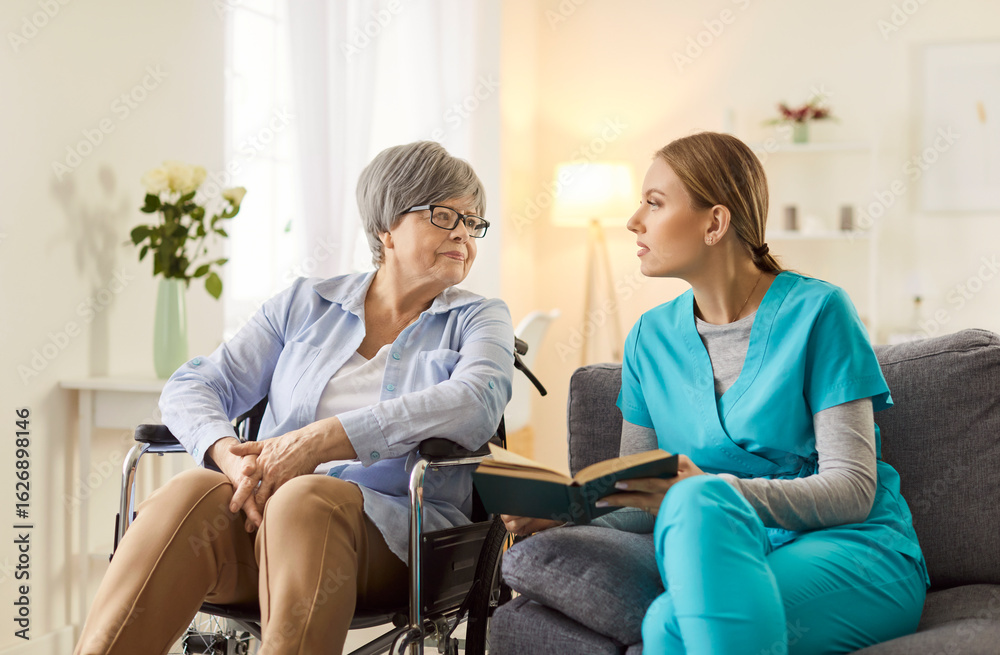 Obraz premium Positive female doctor or nurse reading a book with a senior patient in a wheelchair at a nursing home. Leisure activity fostering companionship, relaxation, and emotional well-being.