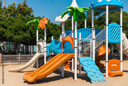 Wallpaper Mural A vibrant playground features colorful slides and climbing structures situated in an outdoor park under clear blue skies. Families enjoy the sunny day surrounded by greenery Torontodigital.ca