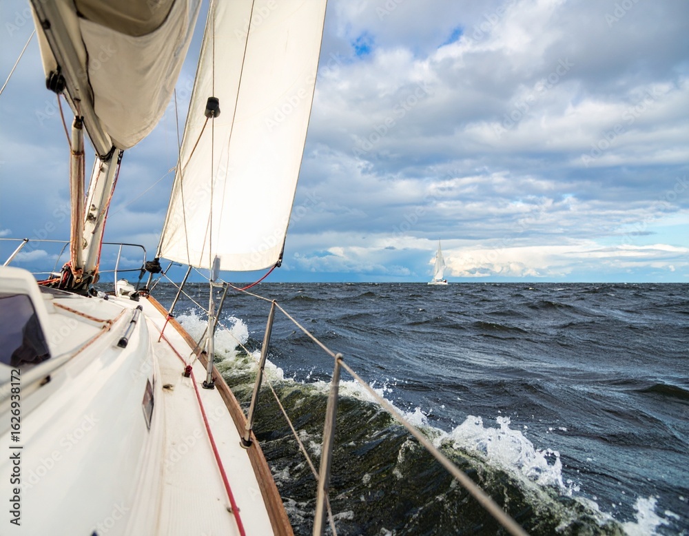 Obraz premium Perspective from white sailboat navigating rough waters with another yacht in distance beneath moody sky. AI-generated