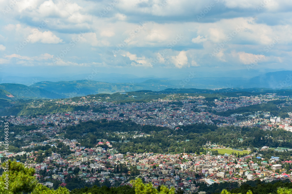 Fototapeta premium Shillong city nestled amidst hills and lush greenery, showcasing a panoramic view under a cloudy sky.