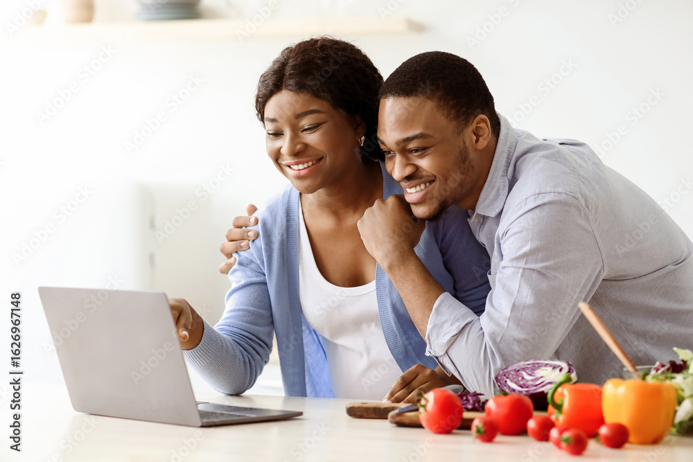 Happy black pregnant couple looking for recipes online, standing in kitchen and looking at laptop screen, copy space. Cheerful african american husband hugging his pregnant wife, cooking together Happy black pregnant couple looking for recipes online, standing in kitchen and looking at laptop screen, copy space. Cheerful african american husband hugging his pregnant wife, cooking together