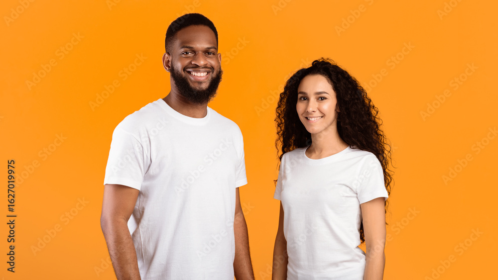Fototapeta premium Multiethnic Couple Posing Wearing White T-Shirts Smiling To Camera Standing Over Yellow Studio Background. Diverse Friendship And Relationship. Happy Multiracial Young Family's Portrait. Panorama