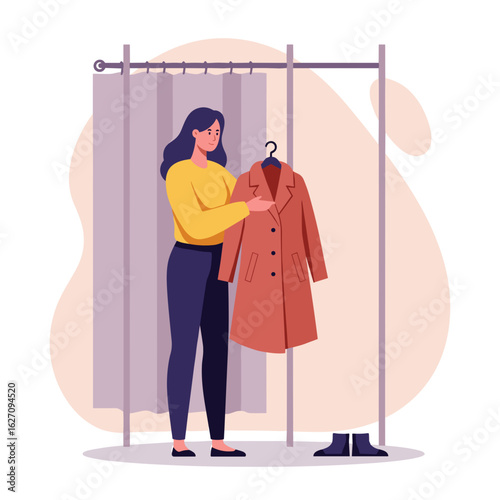 Woman examining coat in fitting room while holding hanger  