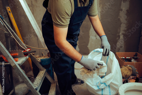 Construction Worker Collects Garbage in Trash Bag at the Working Site. Renovation worker cleaning up messy working space 