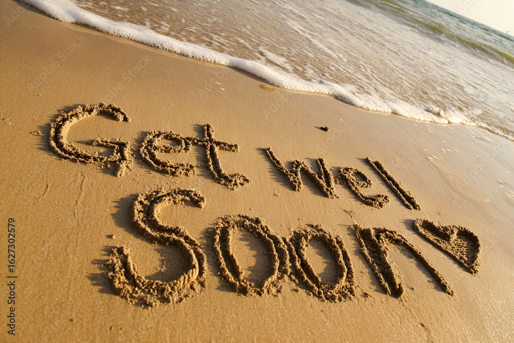 Fototapeta premium Get Well Soon Handwritten in Beach Sand with Minimalist Heart and Cross Illustration and Ocean Foam in Caring Vertical Coastal Scene