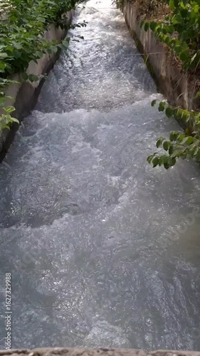 A fast flow of water from a mountain river through a concrete channel among trees