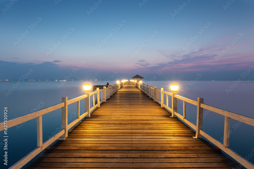 Naklejka premium Seascape in Chonburi Province, Thailand. Glowing lights along wooden bridge under twilight sky, scenic skyline. Architectural construction design in travel destination. Ideal for tourism, landscape.