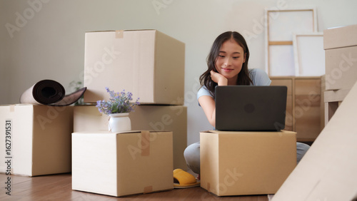 Konstfotografi Asian young adult woman uses laptop computer among moving boxes planning relocat