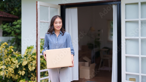 Fotografie Adult Asian woman holds moving box new home entrance smiling homeowner moving da