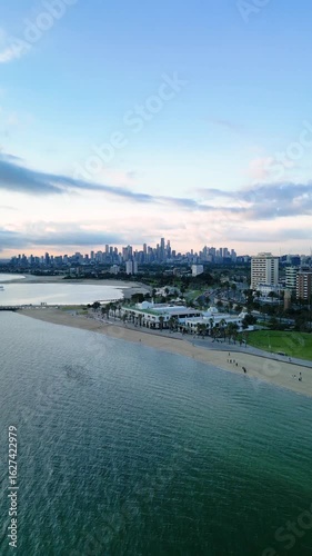 Aerial pull out from Melbourne city skyline and St. Kilda revealing blue calm water of Port Phillip Bay at sunset with pink and blue sky