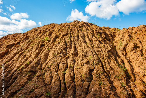 A pile of clay soil dumped by an excavator, an earth embankment against a blue sky