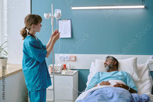 Photos Young adult Caucasian female nurse adjusting IV drip for middle aged biracial ma