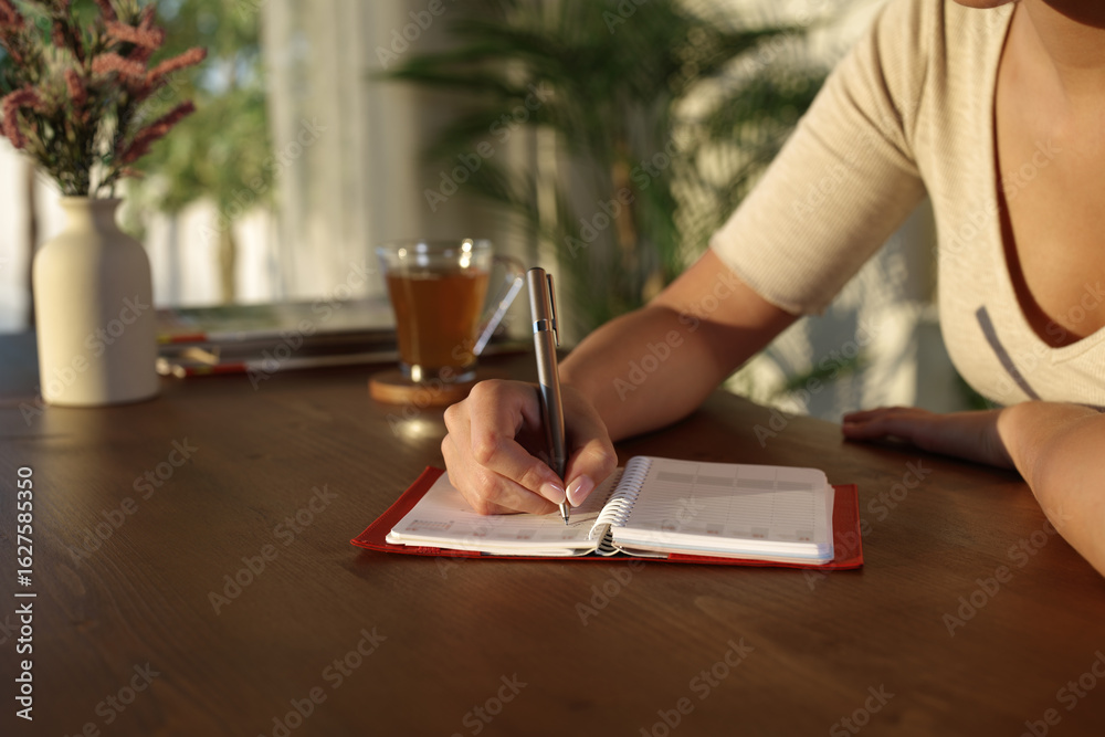 Woman hand at sunset at home writing on agenda Woman hand at sunset at home writing on agenda