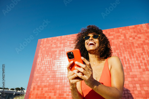 Happy woman laughing while using her mobile phone on a summer day at the beach
