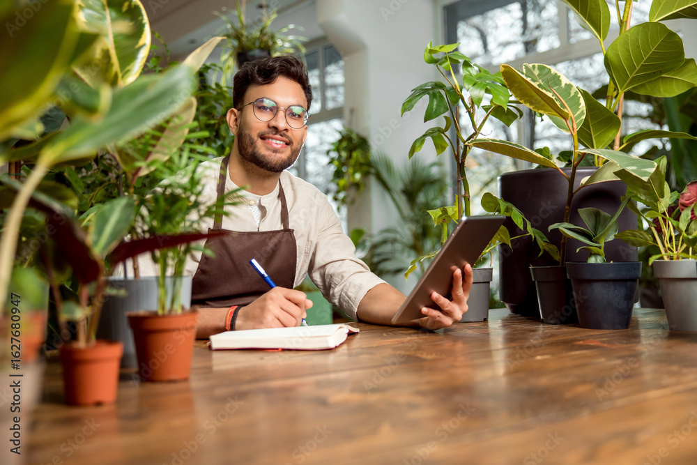 Young male shop assistant making notes while working in the flower shop Young male shop assistant making notes while working in the flower shop