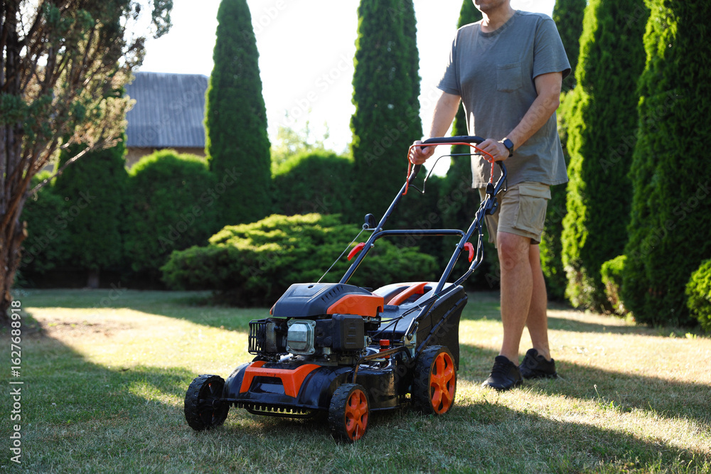 Fototapeta premium Man cutting green grass with lawn mower in garden, closeup