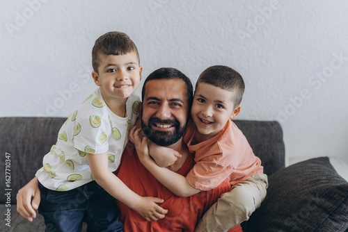 Happy father hugging two smiling sons on a couch. Family bonding moment with kids embracing their dad with love and laughter. Warm, joyful scene of fatherhood and parenting