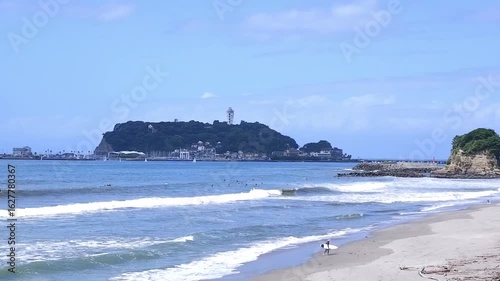 サーファーが波と戯れる夏真っ盛りの湘南・鎌倉の海と、美しい江ノ島の風景で、夏休みのイメージ
