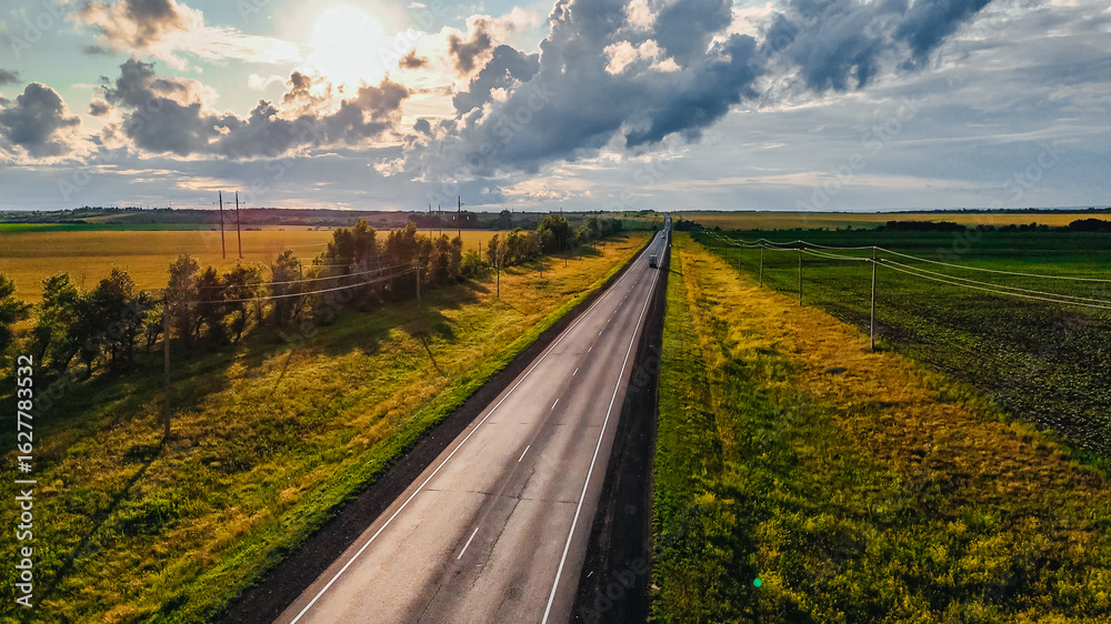 Naklejka premium cars and trucks driving along a highway in the middle of green fields at sunset