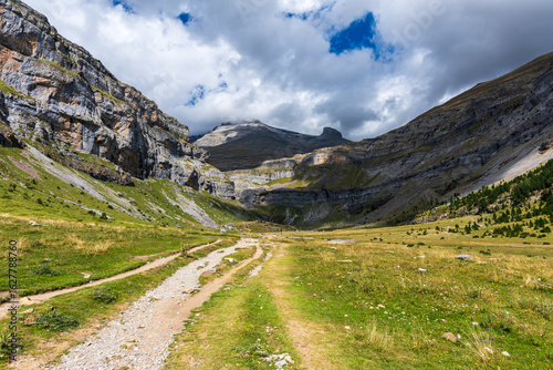 Mountain trail through a dramatic valley under a cloudy sky in late summer. Scenic mountain trail to waterfall in GR11, Ordesa National Park under a shifting sky.