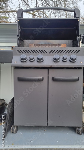 Outdoor barbecue cooker with an open lid standing on a terrace. A modern gas grill, perfect for outdoor cooking and barbecuing. Barbecue gas grill in stainless steel.