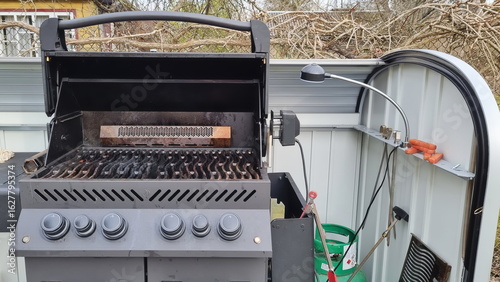 Outdoor barbecue cooker with an open lid standing on a terrace. A modern gas grill, perfect for outdoor cooking and barbecuing. Barbecue gas grill in stainless steel.