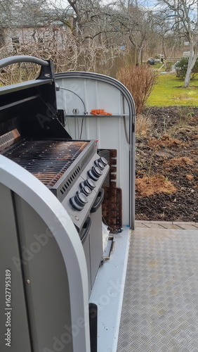 Outdoor barbecue cooker with an open lid standing on a terrace. A modern gas grill, perfect for outdoor cooking and barbecuing. Barbecue gas grill in stainless steel.