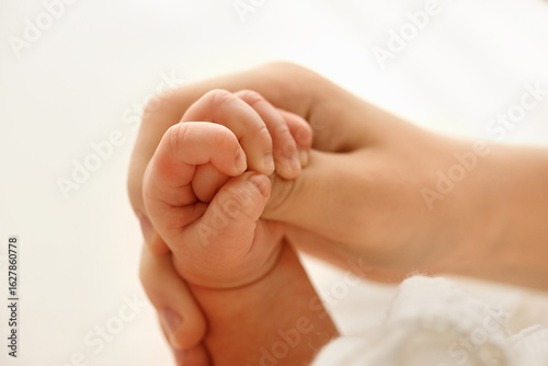 Close-up of a newborn baby tiny hand tightly grasping the mother finger, showing a strong bond, care, and family tenderness on a soft white background.