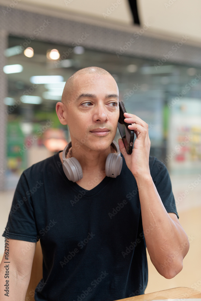Fototapeta premium Man talking on mobile phone alone in mall food court, digital lifestyle concept