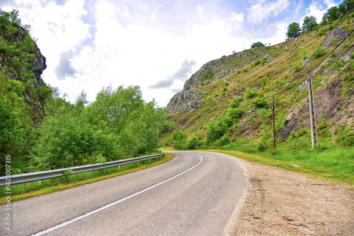 : Carretera asfaltada flanqueada por un desfiladero rocoso y una barandilla roja. Típica ruta de montaña de Transilvania.