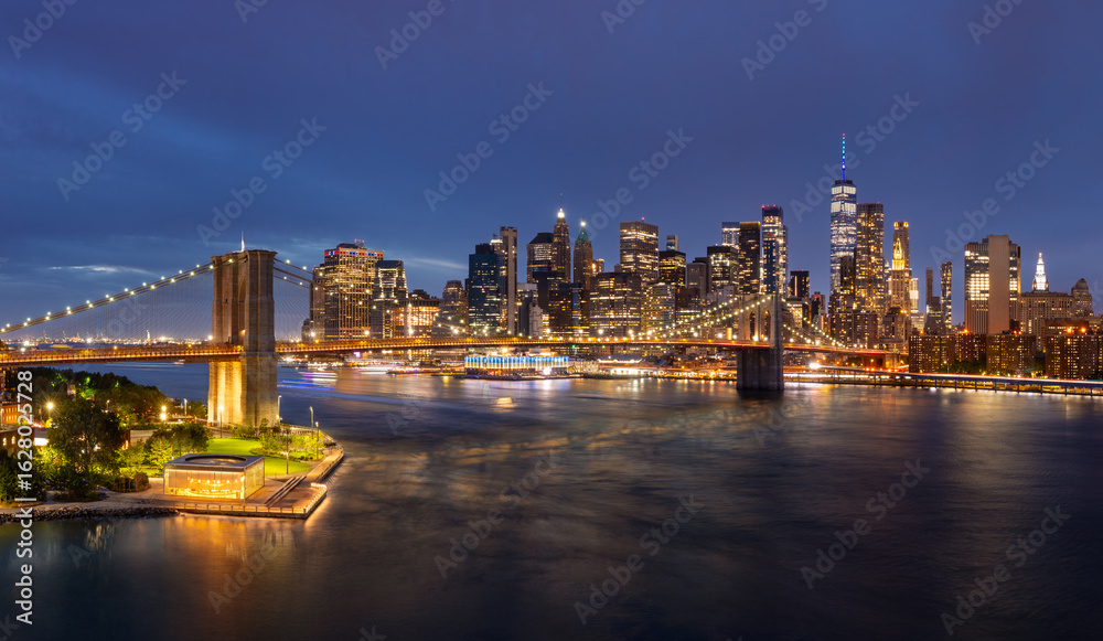 Naklejka premium Elevated view of New York City skyline at dusk with Brooklyn Bridge, Lower Manhattan skyscrapers and East River. Illuminated landmarks and buildings seen from DUMBO at twilight