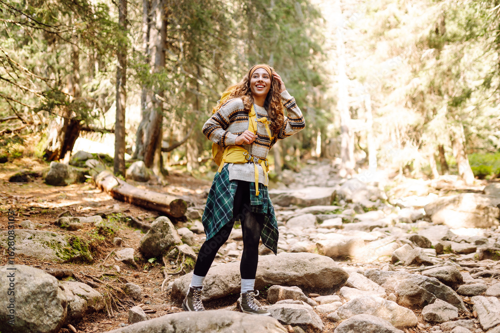 Naklejka premium Female hiker with a colorful hiking backpack on a walking rocky trail in the mountains. Cute woman enjoying mountain scenery in a dense forest. Adventure, hiking and nature concept.