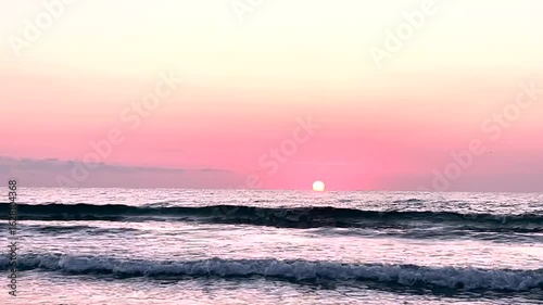 Peaceful sea waves under a pastel pink sunrise sky with the sun touching the horizon. Ideal for meditation videos, travel content, nature backgrounds, or romantic visual themes
