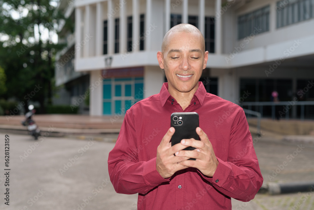 Fototapeta premium Bald man using smartphone while standing outside university building