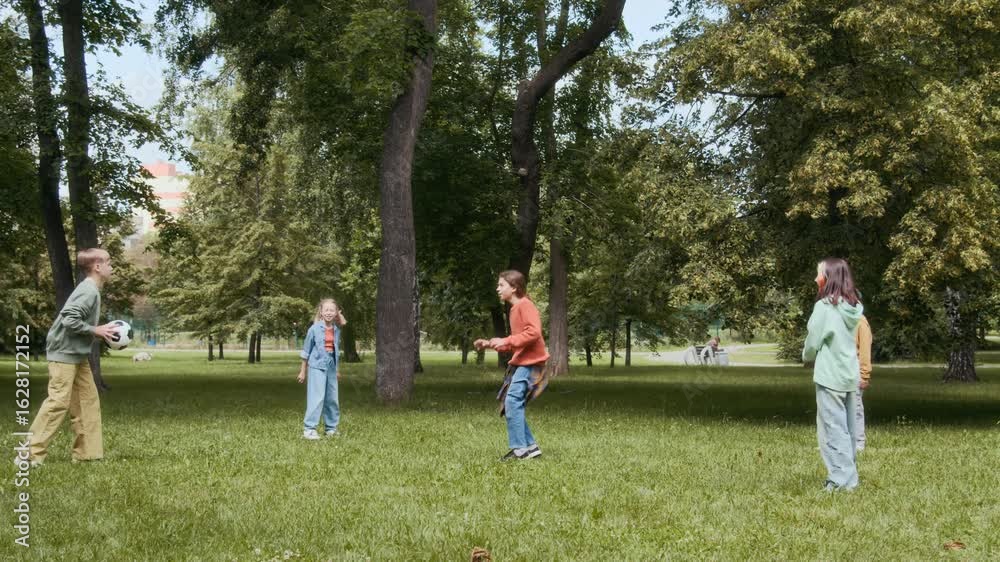 Wide shot of five diverse pre-teenagers throwing ball to one another while playing outdoors with Black male teacher gathering up colourful rings on summer day Wide shot of five diverse pre-teenagers throwing ball to one another while playing outdoors with Black male teacher gathering up colourful rings on summer day