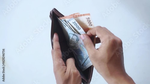 a man's hand is pulling out indonesian money rupiah in a brown leather wallet on a white background