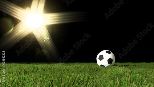 football rests on a pristine green pitch under the dramatic glare of a stadium floodlight at night.