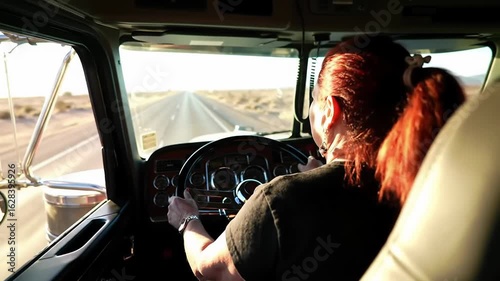 Rear view of female truck driver on long highway. Empowerment and logistics industry concept.
