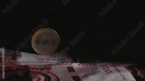 A beam of light illuminates a 1 euro coin on tenge banknotes