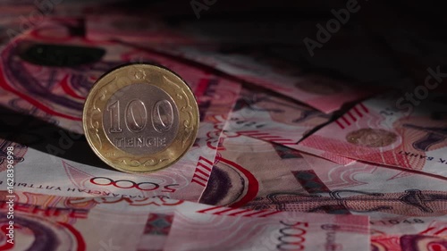 A beam of light illuminates a 100 tenge coin on banknotes