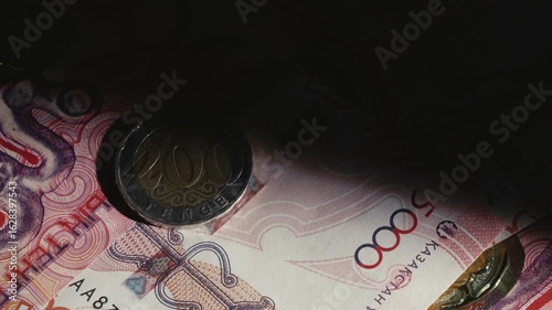 A beam of light illuminates a 200 tenge coin and banknotes