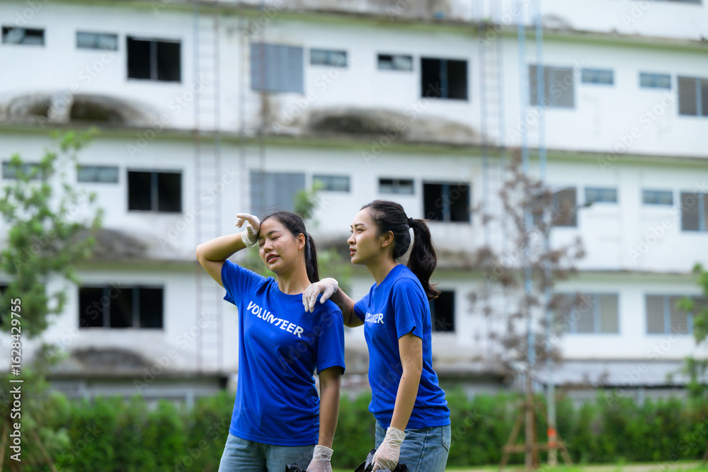 Obraz premium Tired asian volunteers wiping sweat from forehead during social work in front of abandoned building