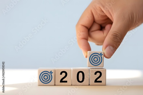 Setting Goals for 2024: A person's hand places a block displaying a target symbol on top of the 202 blocks, symbolizing the commencement of the fresh year, new aspirations, and accomplishments.