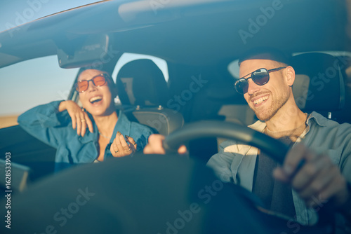 Fotografía Happy couple wearing sunglasses, driving joyfully and laughing together during a