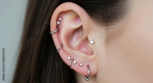 Close-up of a female ear with multiple stylish piercings, including helix and lobe jewelry, showcasing modern body art and fashion trends.
