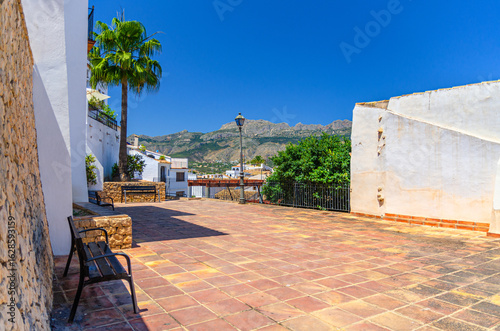 Fototapeta Naklejka Na Ścianę i Meble -  Small square mirador viewpoint with street light and benches, Altea old town typical white houses, mountain range in sunny day, Altea city historical centre Casco Antiguo, Alicante province, Spain