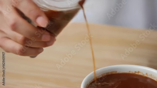 Hand pouring coffee into a white mug on a wooden table  