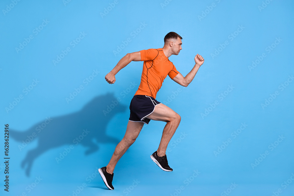 Obraz premium Athletic man running. His shadow in form of hound on light blue background. Sports poster