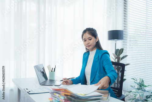 Focused at Work: A dedicated woman is fully engrossed in her work, meticulously reviewing documents, using a laptop, and ensuring attention to detail in a well-lit, organized workspace.